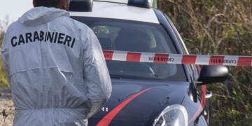 Agente dei Carabinieri in tuta bianca vicino auto blu con nastro segnaletico. Tenta di uccidere compagna a Torino, lei scappa dai vicini con la bimba e si salva. Lui poi si suicida