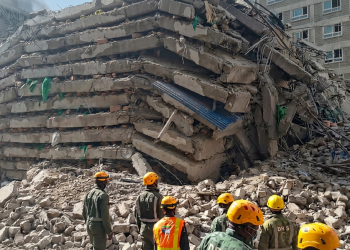 Soccorritori con caschi gialli osservano le macerie dell'edificio crollato. Nairobi, crolla un palazzo di oltre 10 piani: persone intrappolate sotto le macerie