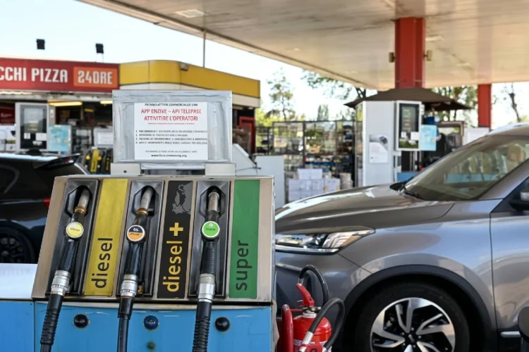 Pompa di benzina a un distributore carburante con erogatori e auto grigia.