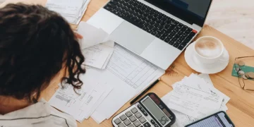 Giovane calcola tasse e fatture su scrivania con computer e telefono.