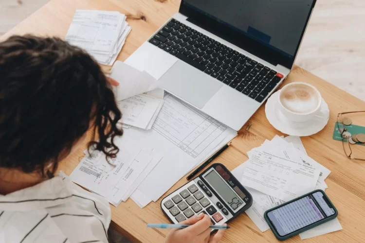 Giovane calcola tasse e fatture su scrivania con computer e telefono.