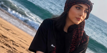 Giovane donna sorride sulla spiaggia con copricapo scuro e rosso