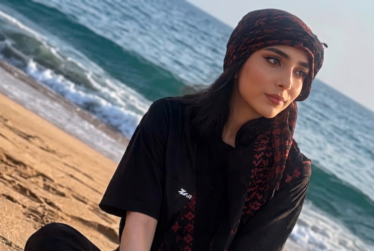 Giovane donna sorride sulla spiaggia con copricapo scuro e rosso