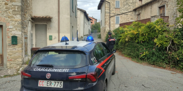Auto dei Carabinieri parcheggiata in una strada tra case in pietra. Tortona, bimba di 3 anni trovata morta in casa: arrestata la madre