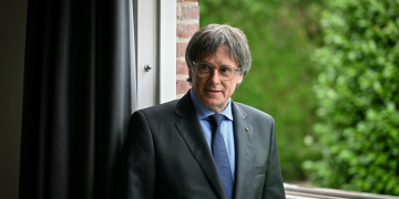 Carles Puigdemont in abito scuro guarda pensieroso fuori da una finestra. Puigdemont può tornare in Spagna: il Tribunale Supremo revoca l'ordine di arresto