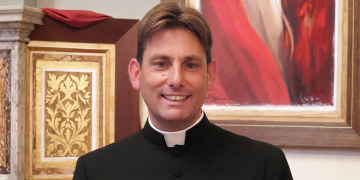 Don Antonio Coluccia sorride, indossa abito talare nero, colletto bianco. Accerchiato e minacciato don Coluccia, il prete antispaccio di Roma: denunciati 3 tunisini