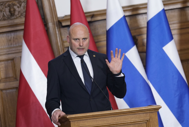 Kariņš, Primo Ministro lettone, parla al podio con bandiere europee.Lettonia, Lista Unita conquista 42 seggi e segna il miglior risultato nelle elezioni per un partito dal 1991